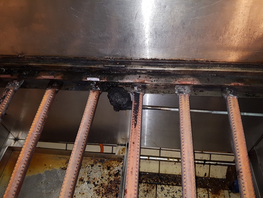 Gas burner bars covered in burnt-on carbon deposits before treatment